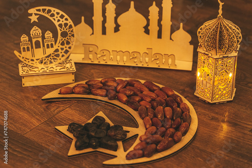 Ramadan Kareem. Dates on wooden tray in the shape of a month and a star and oriental wooden Lantern lamps on wood background. Islamic Holy Month Greeting Card. Soft focus. Shallow DOF.