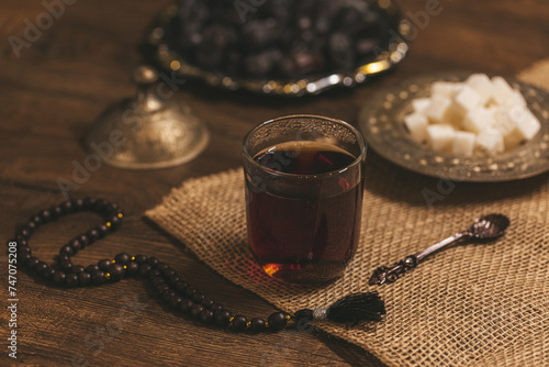 Glass of tea with sugar and dried dates on a wooden background with burlap. Ramadan Kareem . Islamic Holy Month Greeting Card. Soft focus. Shallow DOF.