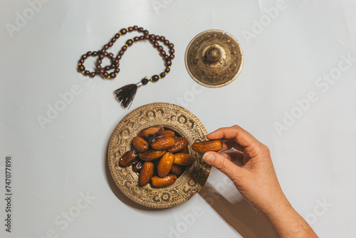 Bronze plate with dried dates, wooden rosary and date in a woman's hand. Ramadan Kareem holiday concept