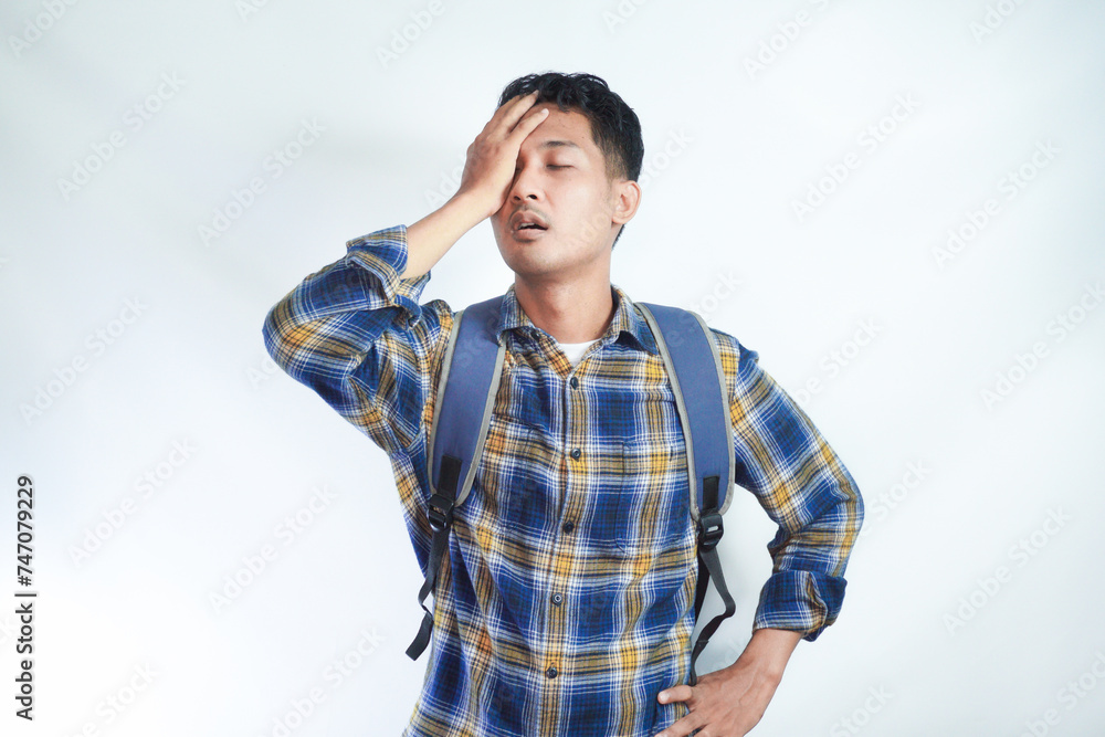 Confused young Asian student man wearing casual clothes with backpack covering his face with hand isolated on white background. High school university college concept Confused young Asian student man wearing casual clothes with backpack covering his face with hand isolated on white background. High school university college concept