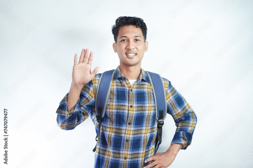 Smiling young Asian male student from college in casual clothes with a backpack, saluting a friend with hand isolated on white background. Education in high school university college concept Smiling young Asian male student from college in casual clothes with a backpack, saluting a friend with hand isolated on white background. Education in high school university college concept