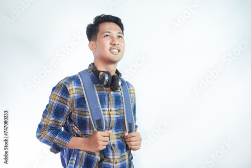 Cheerful young Asian man student in casual clothes backpack looking on empty space, new advertisement for school enrollment isolated on white background. high school university college concept © AriaSandi