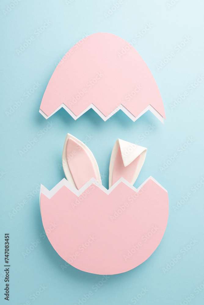 Charming Easter imagination brought to life. Vertical top view captures whimsical rabbit ears peeking from an eggshell on a gentle blue background, with space for text or promotion Charming Easter imagination brought to life. Vertical top view captures whimsical rabbit ears peeking from an eggshell on a gentle blue background, with space for text or promotion