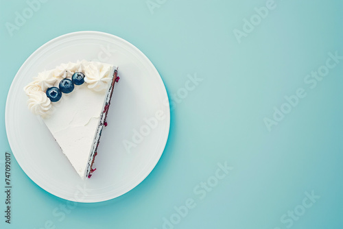 Triangular piece of sponge cake with whipped cream and blueberries on a plate on a blue background. Copy space. Top view.