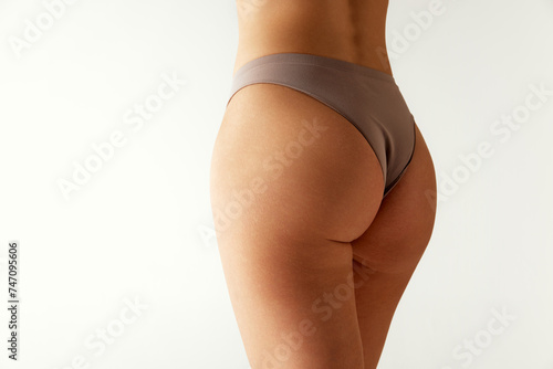 Rear view of female body, legs, buttocks in neutral-tone underwear against grey studio background. Body positivity. Concept of beauty treatments, dieting, female health, spa procedures. Ad