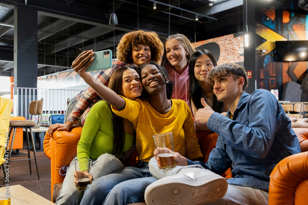 Naklejka premium Happy friends taking selfie photo at brewery restaurant - Group of multiracial people enjoying happy hour in arcade - Lifestyle concept with guys and girls hanging out