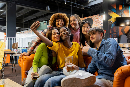 Happy friends taking selfie photo at brewery restaurant - Group of multiracial people enjoying happy hour in arcade - Lifestyle concept with guys and girls hanging out photo