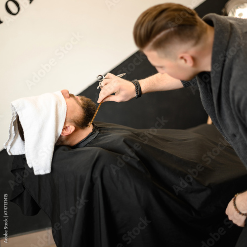 Barber combs beard with comb while shaving Caucasian man photo