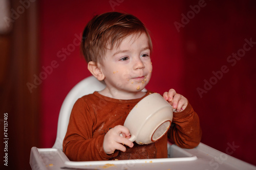 A hungry toddler affectionately 'kisses' the bottom of an empty bowl, capturing a moment of adorable greediness after a satisfying meal photo