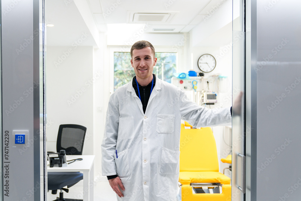 Friendly doctor in lab coat inviting into his well-equipped clinic room.