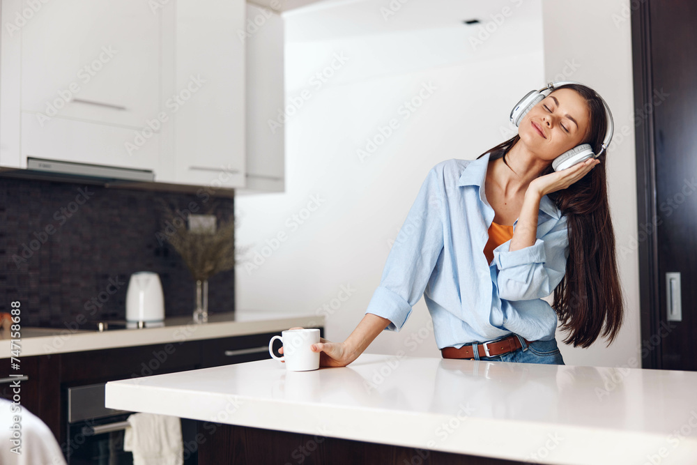 Woman enjoying music with coffee in kitchen while sitting on counter with coffee cup Woman enjoying music with coffee in kitchen while sitting on counter with coffee cup