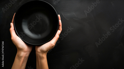 Woman hand holding blank black bowl on black background