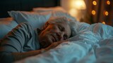 An elderly woman with closed eyes peacefully sleeping on a bed with white sheets and pillows under a soft light.
