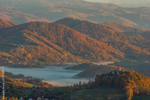 Beautiful mountainous rural landscape in autumn morning. Aerial view of landscape of mountains and hills with fog at sunrise in autumn colors. © Ivan