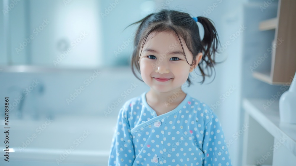 A young girl with pigtails wearing a blue polka dot pajamas standing in a bathroom with a smile on her face. A young girl with pigtails wearing a blue polka dot pajamas standing in a bathroom with a smile on her face.