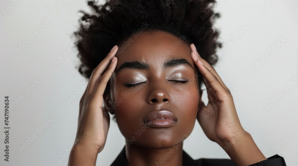 Fototapeta premium A woman with closed eyes resting her hands on her temples conveying a sense of relaxation or meditation.