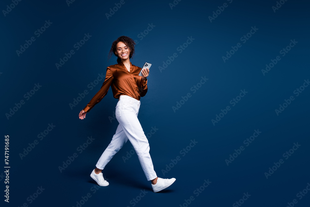 Full length photo of positive shiny woman dressed brown silk shirt chatting twitter telegram facebook empty space isolated blue color background Full length photo of positive shiny woman dressed brown silk shirt chatting twitter telegram facebook empty space isolated blue color background