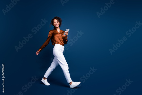 Full length photo of positive shiny woman dressed brown silk shirt chatting twitter telegram facebook empty space isolated blue color background