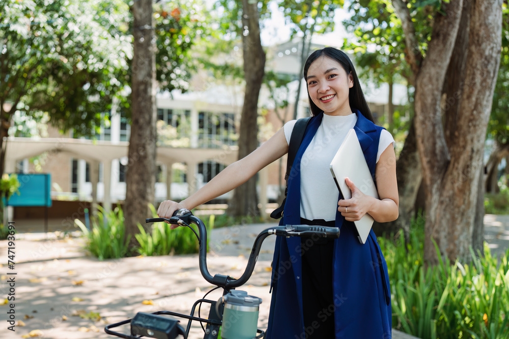 Obraz premium Young businesswoman sitting on stair in city park and using laptop for work hybrid. Bike to work eco friendly alternative vehicle green energy