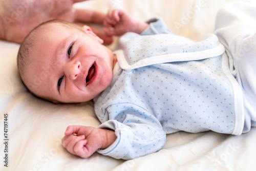 A wide-awake newborn baby in a patterned onesie lies on a soft surface, gazing with curious eyes and a partially open mouth photo