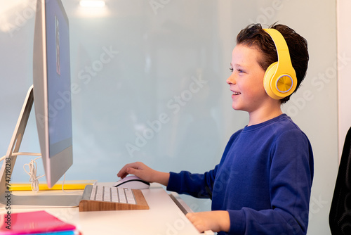 A cheerful child interacts with a computer, wearing bright yellow headphones, with a smile indicating enjoyment or success with the task at hand photo