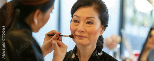 Makeup artist applies powder and blush . Beautiful mature Asian Woman face. Hand of make-up master puts blush on cheeks beauty model girl . Make up in process . Beautiful woman