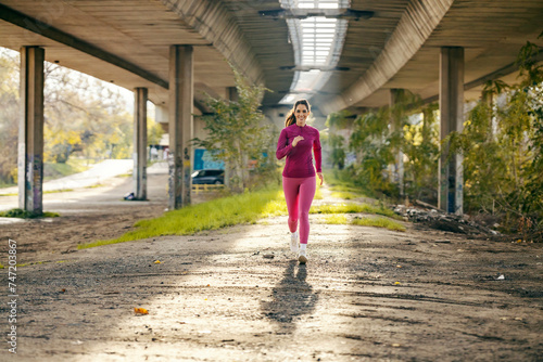 A fit sportswoman is running under the bridge.