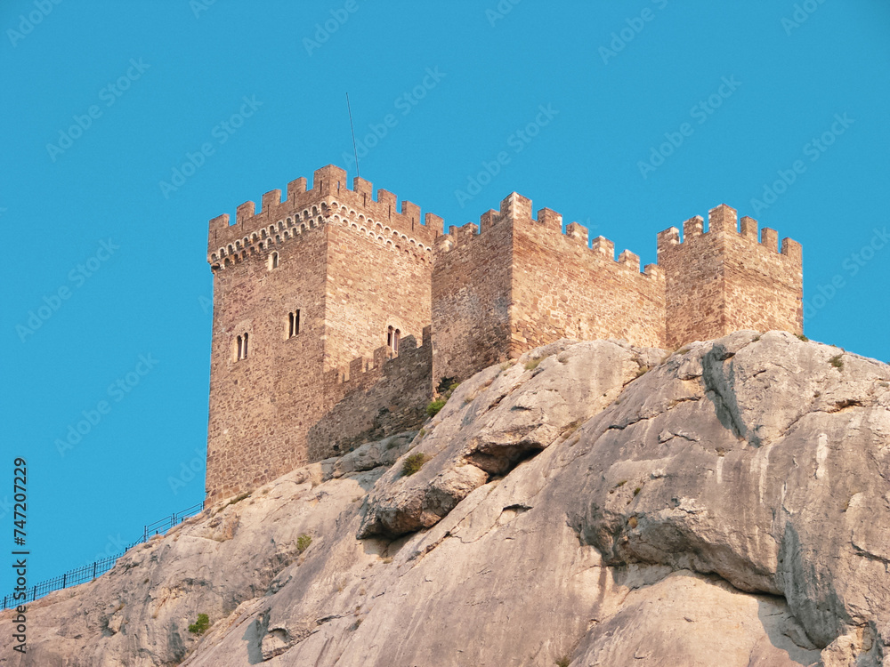 A medieval fortress on a stone rock against the background of a clear blue sky.