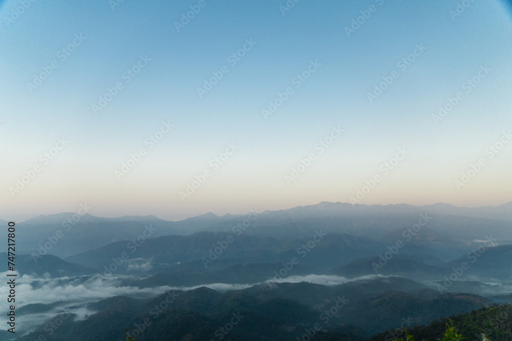 Misty mountain landscape, clear blue cloudless sky and layers of hills. Cold mood.