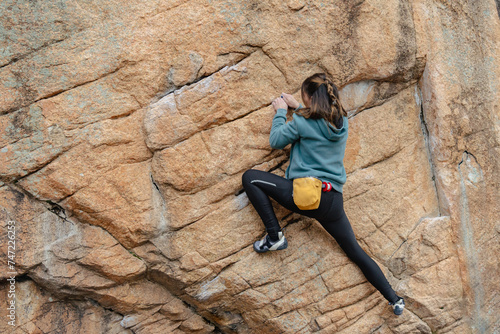 A focused female climber with a chalk bag strategically maneuvers on a steep boulder face during an outdoor climb photo