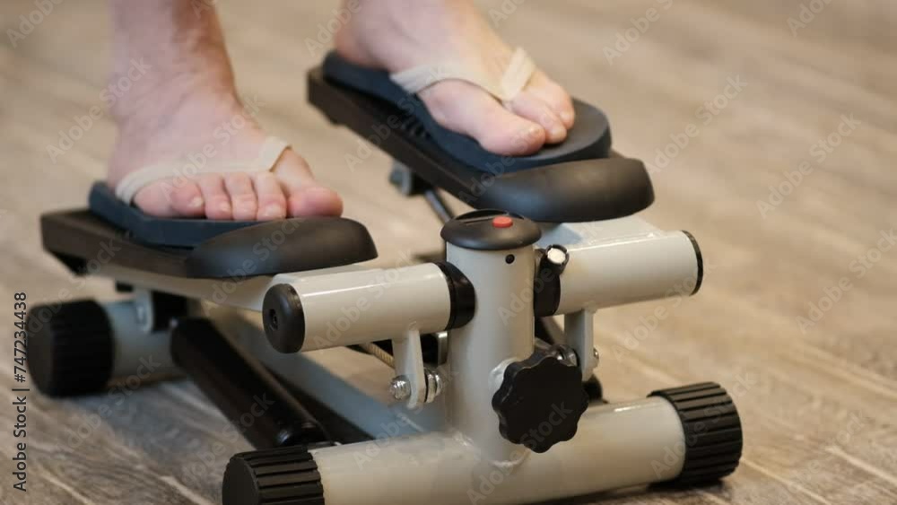 A young man on a mini stepper does a leg warm-up. Modern lifestyle, indoor sports A young man on a mini stepper does a leg warm-up. Modern lifestyle, indoor sports