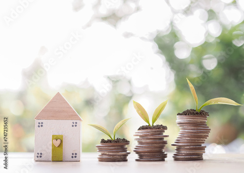 Miniature house and plants growing up on stack of coins. The concept of saving money for house, Property investment, House mortgage, Real estate.