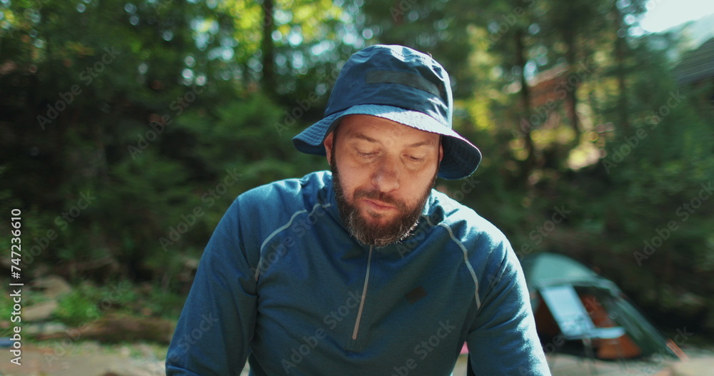 A male traveler has set up camp in the forest and is eating while sitting in front of the tent. Travel, hiking and camping concept happy man camping in forest. A male traveler has set up camp in the forest and is eating while sitting in front of the tent. Travel, hiking and camping concept happy man camping in forest.