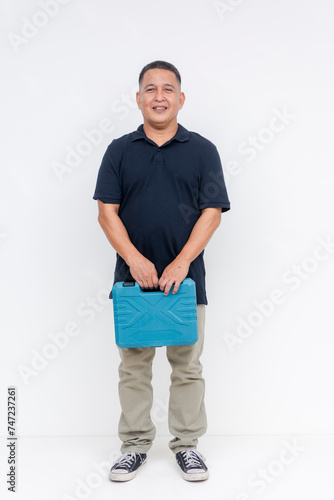 Full body photo of a smiling middle aged Asian man casually holding a blue toolbox, standing against an isolated white background.
