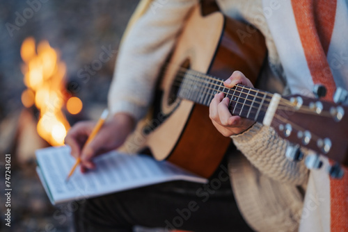 Close up on acoustic guitar of a girl guitarist composing new song. Young musician playing the guitar outdoors in the evening near bonfire