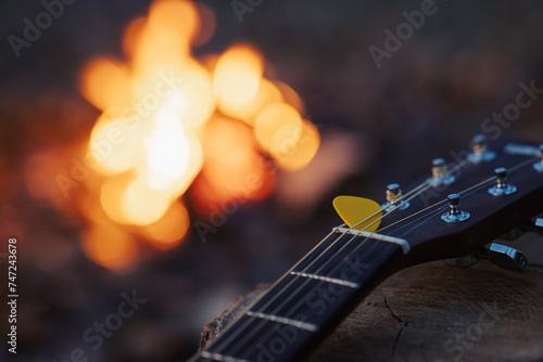 Close up on yellow mediator on guitar with bonfire on the background. Playing guitar, music, having good time camping on nature
