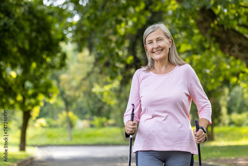 Active senior woman enjoying nordic walking exercise in lush park