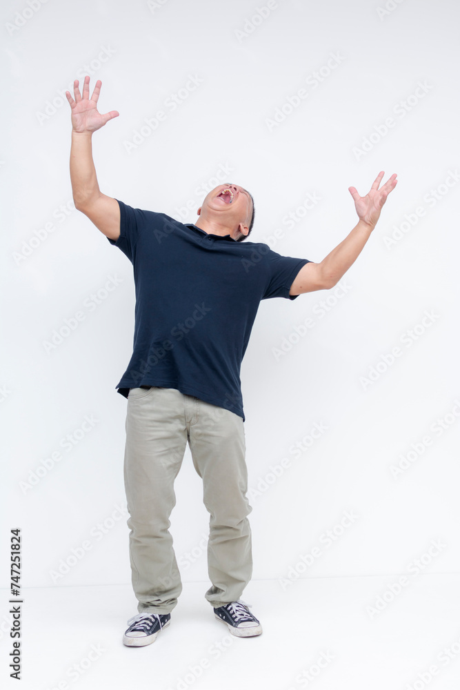 Naklejka premium Full body shot of a middle-aged Asian man screaming loudly with his arms up in the air, against a white backdrop.