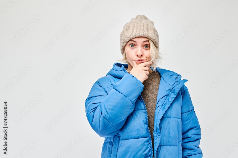 Woman in winter attire looking thoughtful against a light background. Woman in winter attire looking thoughtful against a light background.