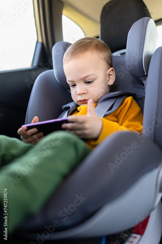 Little boy using smart phone while sitting in car back seat.