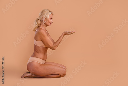 Photo of attractive middle aged lady sitting hold spa salon procedure ads on empty space isolated over pastel color background © deagreez