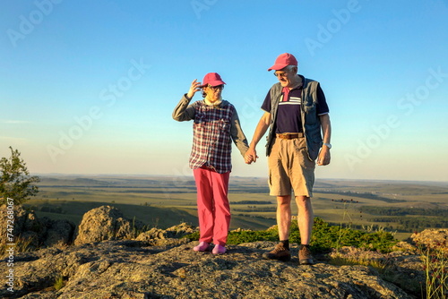 a beautiful mature couple on a high rock admires the Ural nature and the Ai river on a summer sunny day