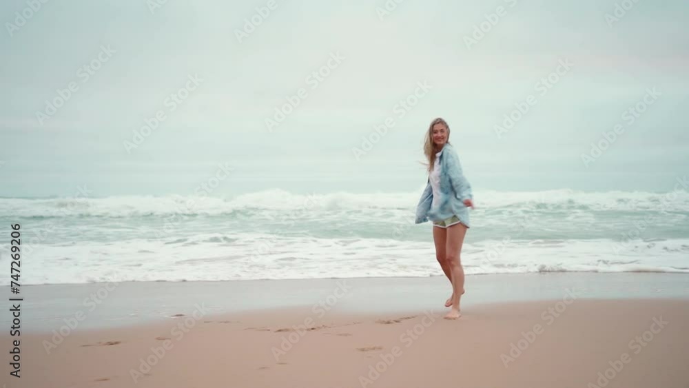 Happy woman running ocean beach and turns around, smiling at camera. Happy female traveler dressed denim shirt walk sandy sea beach, holiday vacation Happy woman running ocean beach and turns around, smiling at camera. Happy female traveler dressed denim shirt walk sandy sea beach, holiday vacation
