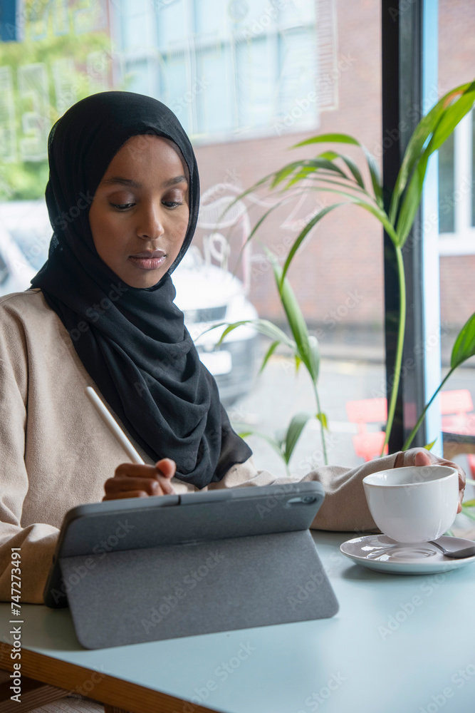 Young woman in hijab working on tablet in cafe Young woman in hijab working on tablet in cafe