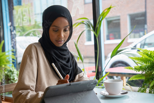 Photography Young woman in hijab working on tablet in cafe