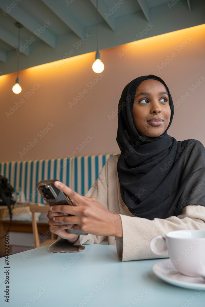 Smiling young woman in hijab using phone in cafe Smiling young woman in hijab using phone in cafe