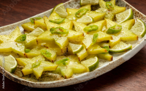 Homemade carambola or star fruit spicy salad with green chili, lime pieces, and lime juice. Perfect condiment for grilled fish or a curry. Wooden table.