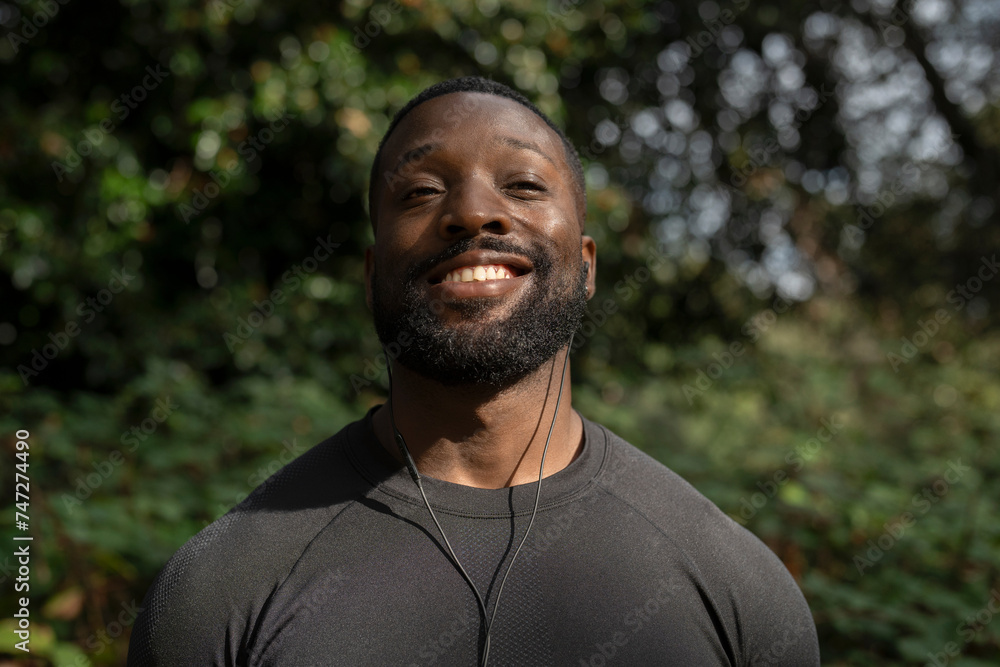 Portrait of smiling athletic man with earbuds standing in park Portrait of smiling athletic man with earbuds standing in park