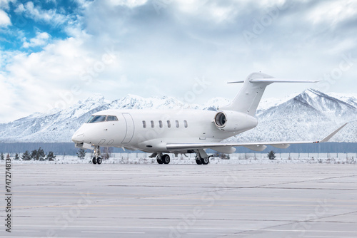 White luxury executive airplane taxiing on airport taxiway in winter on the background of high picturesque snow capped mountains