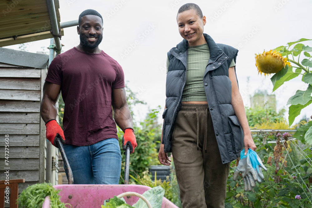 Obraz premium Smiling couple with vegetables in wheelbarrow in urban garden
